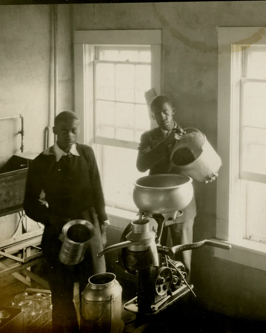 Two African American men work with vintage dairy equipment inside a creamery, representing N.C. A&T's historic dairy program. Overlay text highlights the university's legacy, stating it opened its dairy unit in 1897 and remains the only HBCU with an active dairy unit today.